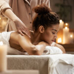Tender african girl smiling enjoying massage with closed eyes in spa resort.
